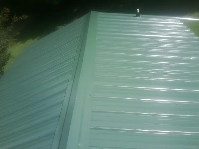 New green metal panels meeting at the ridge of a roof — Flat Roof Repair work by our crew in Ely