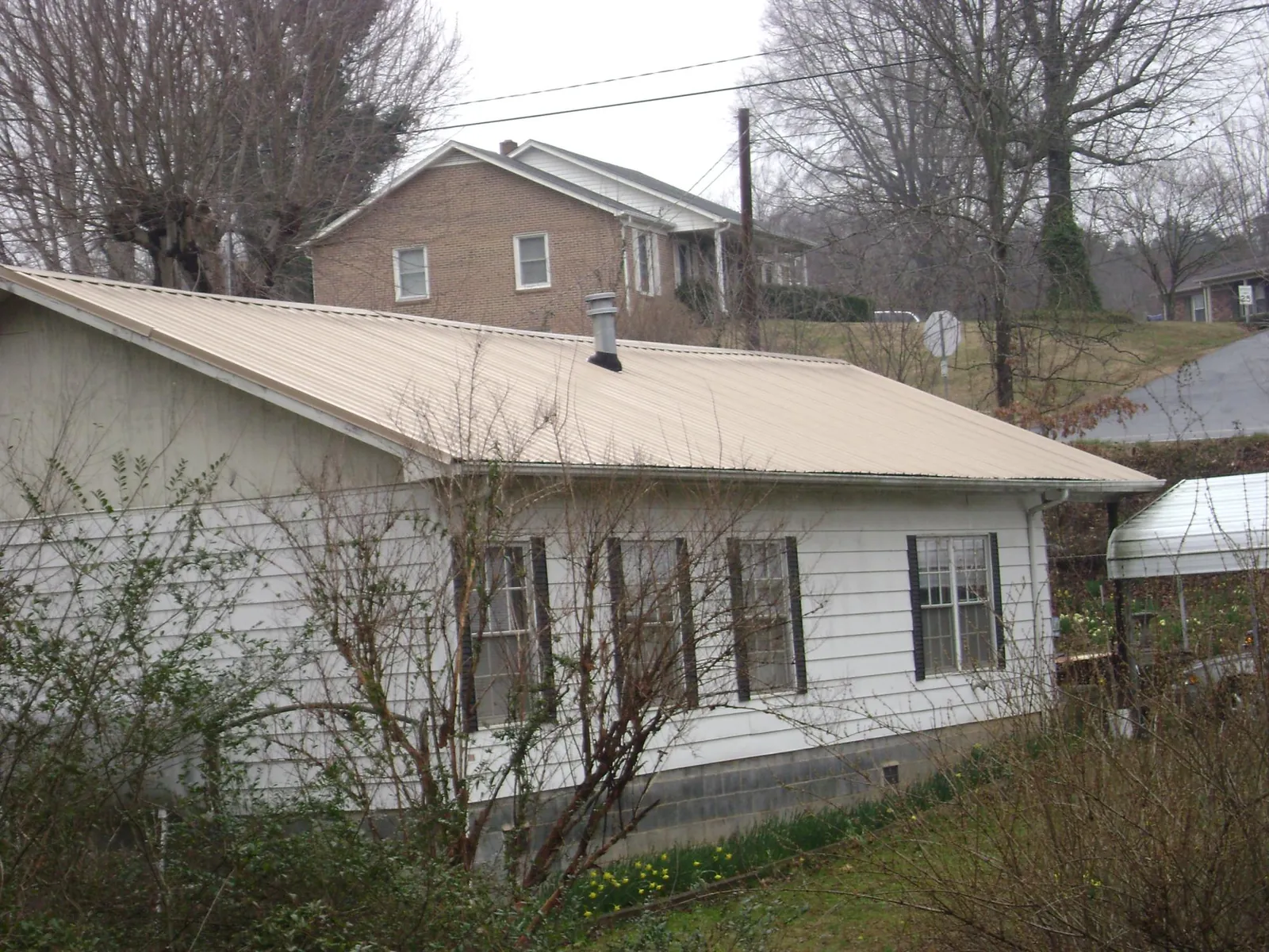 Tan metal roof on a white sided house set into a hillside — Commercial Roofing by Roofing Brothers in Ely